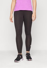 Svarta leggings i stretchigt material, åtsittande design, med en logo på underbenet. Kombinerat med en rosa t-shirt och svarta löparskor.