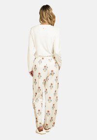 White long-sleeve top paired with cream pants featuring colorful floral patterns. Loose-fitting with an elastic waistband and soft texture.