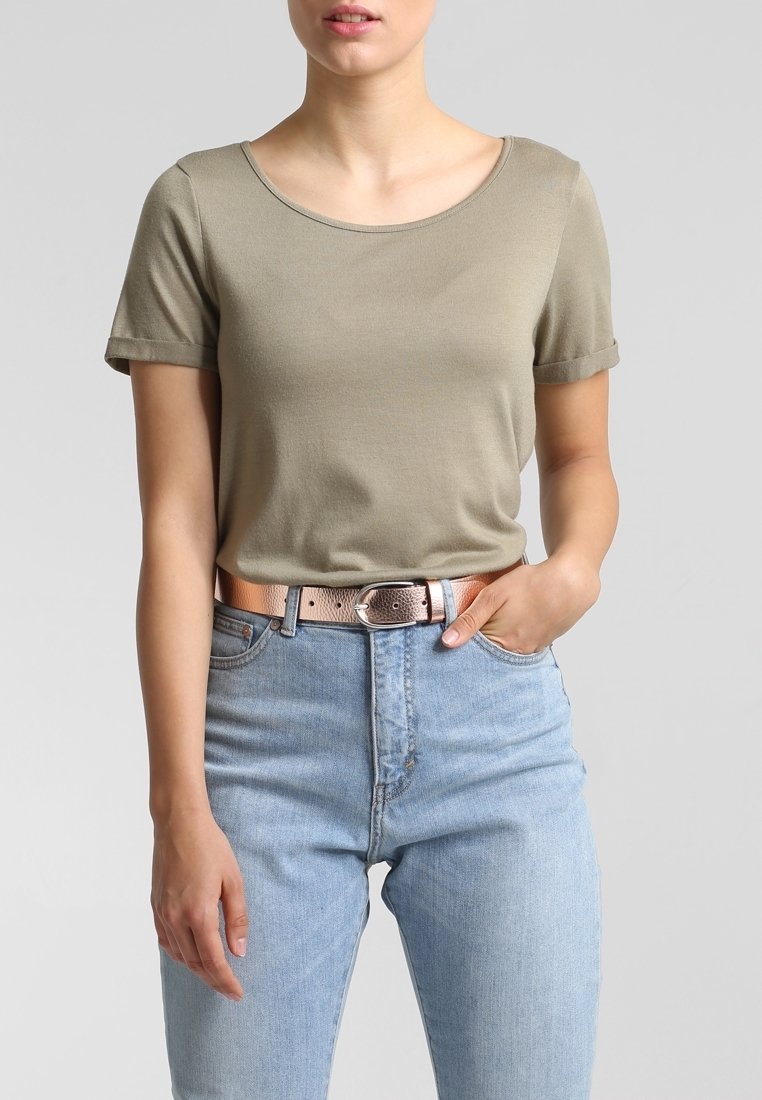 Femme portant une chemise à manches courtes marron clair rentrée dans un jean taille haute bleu clair avec une ceinture métallique bronze.