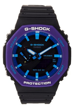 Schwarze und lila Casio G-Shock Uhr mit blauen Stundenmarkierungen und Zeigern, Digitalanzeige und beschrifteten Funktionsknöpfen auf der Lünette.