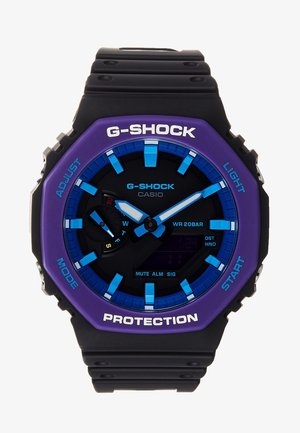 Czarny i fioletowy zegarek Casio G-Shock z niebieskimi markerami godzin i wskazówkami, wyświetlaczem cyfrowym oraz oznaczonymi przyciskami funkcyjnymi na pierścieniu.