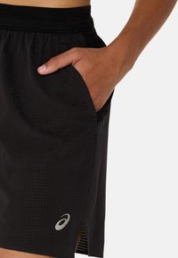 Black athletic shorts made of lightweight material with a grid texture, featuring a side pocket and a logo near the hem.