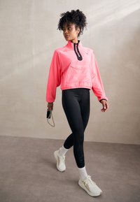 Veste zippée rose fluo avec des accents noirs, poche avant, assortie à des leggings noirs avec un détail léopard et des baskets blanches.