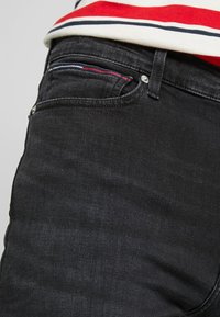 Jeans de mezclilla negra con un diseño clásico de cinco bolsillos, costuras en contraste en el pequeño bolsillo frontal y una silueta ajustada.