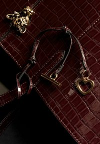 Geantă din piele cu imitație de crocodil burgundy, cu o curea din piele neagră, un charm în formă de inimă de culoare aurie și un accent decorativ din hardware aurit.