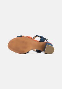 Sandal dengan hak dan tali suede berwarna-warni, nuansa oranye dan biru tua, sol halus, dan bagian bawah yang bertekstur untuk cengkeraman. Tali pergelangan kaki yang dapat disesuaikan.