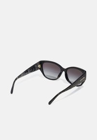 Schwarze Sonnenbrille mit kantiger Cat-Eye-Form; graue Verlaufslinsen; marmorierte, schwarz akzentuierte Bügel mit goldfarbenem Logo-Detail.