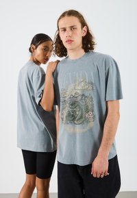 Camiseta gráfica de algodón gris con un diseño de paisaje desértico y texto, de mangas cortas, corte relajado, combinada con pantalones cortos de ciclismo negros.