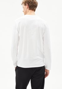 Witte katoenen t-shirt met lange mouwen en een ronde halslijn, een gladde textuur en een rechte onderkant, gedragen met zwarte broek. Geen zichtbare patronen.
