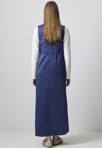 Rochie lungă de culoare albastru închis, cu o talie strânsă, confecționată dintr-un material neted. Prezintă un design fără mâneci și are o tăietură până la podea.