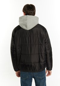 Sort dunjakke med grå hætte. Har et quiltet design, elastisk kant og sidelommer. Enkel, funktionel stil.