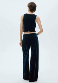 Satiini tummansininen cropped toppi ja siihen sopivat korkeavyötäröiset leveälahkeiset housut. Suora pinta, yksinkertainen muotoilu, eikä näkyviä kuvioita tai varusteita.