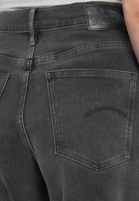 Donkergrijze spijkerbroek van denim met een subtiele textuur. Opvallende accenten zijn een leren label en twee achterzakken met kenmerkende stiksels.