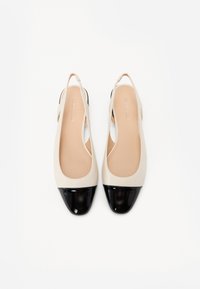 Ballerines beiges à talon ouvert avec un embout en cuir verni noir. Matière lisse, pointe en amande et design à talon ouvert.