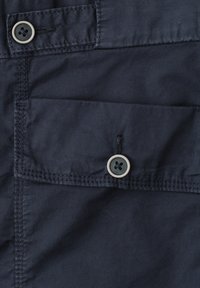 Tissu bleu marine foncé en gros plan montrant une poche à rabat boutonnée avec des coutures visibles et deux boutons assortis à quatre trous.