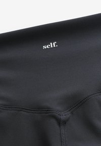 Must must verfügen smooth kanga, mis sisaldama tonal õmblused ja väike valge logo "self." kaela lähedal.