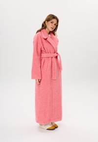Flauschiger rosa Morgenmantel mit einem Schalkragen, langen Ärmeln und einem passenden Gürtel. Er hat eine mittlere Länge bis zur Wade und eine weiche Textur.