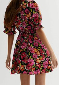 Robe fleurie avec un fond noir et de vibrantes fleurs roses, oranges et vertes. Manches courtes et bouffantes avec un lien à la taille.