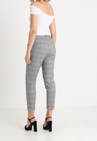 Grå rutig byxa med tapered fit, hög midja och bältesöglor, som bärs med en vit off-shoulder topp och svarta högklackade sandaler.