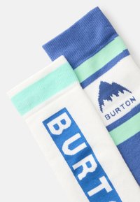 Dois pares de meias: uma em branco com lettering azul, a outra em riscas azuis e verdes com um logótipo de montanha. Material suave e de malha.