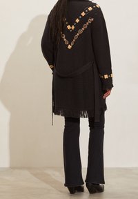 Black knitted cardigan with floral embroidery in yellow and red. Features a V-shaped design, frayed hem, and a tied belt.