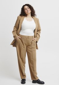 Tan streepjasje met een gestructureerde blazer en losse broek. Witte tanktop met kant aan de rand eronder. Glanzende zwarte schoenen maken de look af.
