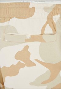 Tan and beige camo-patterned shorts with a smooth texture; features an elastic waistband and a rear pocket with a simple flap design.