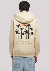 Cream hoodie featuring a black palm tree graphic and an orange sun on the back, with the text "ESCAPE AND DISCOVER THE WORLD" beneath.