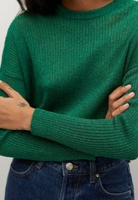 Vihreä ribbineulottu rento istuvuusneule, jossa on pyöreä pääntie ja pitkät hihat, yhdistetty sinisiin farkkuihin.