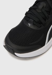 Sneakers de sport noirs avec une tige en mesh respirant, accentués par un logo blanc et un design élégant, dotés de lacets texturés et d'une semelle en caoutchouc.