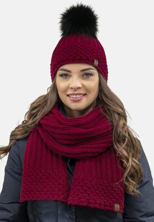 Maroon knitted beanie and scarf set featuring a textured pattern, with a black faux fur pom-pom on the hat. Soft, warm texture.