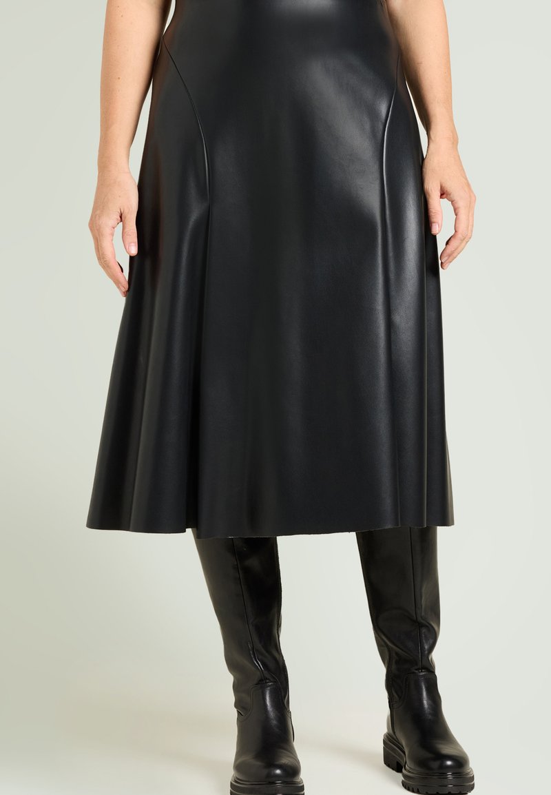 Sort læder A-formet nederdel med glat tekstur, lodrette sømme og udvidet kant. Kombineret med knælange sorte læderstøvler.