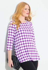 Top viola con grandi pois bianchi, scollatura rotonda, maniche 3/4, abbinato a una pochette nera e leggings neri, tessuto liscio.