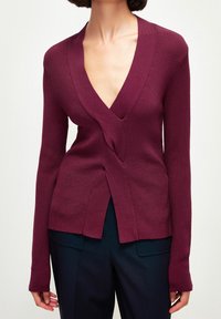 Cardigan en maille bordeaux avec un col en V profond, des manches longues, et un design torsadé à l'avant, présentant une texture côtelée et un ourlet ouvert.