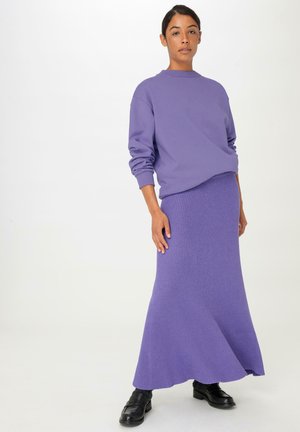 Lila Langarm-Sweatshirt, kombiniert mit einem passenden gerippten Maxirock. Das Outfit besitzt einen lässigen Schnitt und ein strukturiertes Material, ergänzt durch schwarze Schuhe.