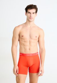 Piros pamut boxer alsónadrág, puha elasztikus derékpánttal, amelyen a "Calvin Klein" felirat található. A dizájn szoros illeszkedést és sima textúrát kínál.