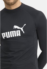 Schwarzes langärmliges Sportshirt mit hohem Kragen. Es verfügt über ein großes weißes Puma-Logo auf der Brust und einen glatten, dehnbaren Stoff.