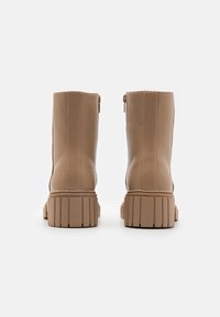 Botas de tobillo de imitación cuero en tono marrón claro con una cremallera forrada en la parte trasera y una suela gruesa y estriada. Acabado liso sin detalles visibles.