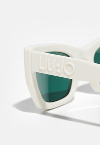 Occhiali da sole oversize bianchi con lenti verdi. Presentano una montatura spessa e un design frontale piatto. Logo "LIU•JO" impresso sulla stanghetta.