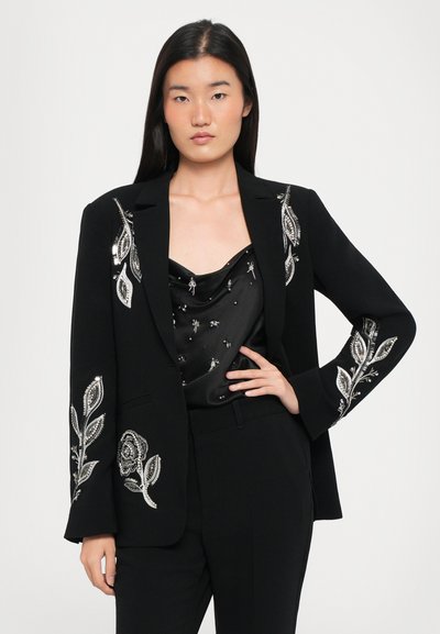 Black blazer with silver floral embroidery on sleeves, worn over a black satin top featuring subtle embellishments. Tailored fit and clean lines.