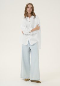 White button-up shirt with oversized fit, long sleeves. Light blue wide-leg jeans. Brown suede shoes. Simple, minimalistic design.