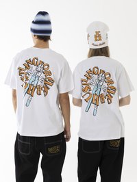 Weiße Baumwoll-T-Shirts mit bunten Grafikdrucken auf dem Rücken, kombiniert mit schwarzen, weiten Hosen. Die Accessoires umfassen eine weiß-blau gestreifte Mütze.