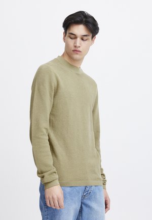 Olive green textured sweater with a crew neck, ribbed cuffs, and a fitted silhouette, paired with light blue jeans.