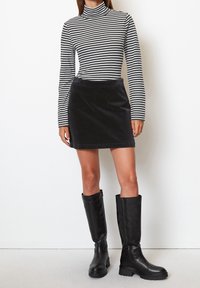 Mini gonna in corduroy nera abbinata a un dolcevita a righe bianche e nere. Il modello indossa stivali alti neri in pelle con suola spessa.