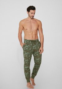Pantalones de chándal verde camuflaje con cinturilla ajustable, puños acanalados y bolsillos laterales; fabricados en tejido suave, diseñados para la comodidad.