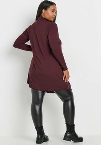 Mörkröd ribbad tunika med hög halsringning, texturerat tyg och vågigt fåll, tillsammans med svarta fusk-läder leggings och kängor.