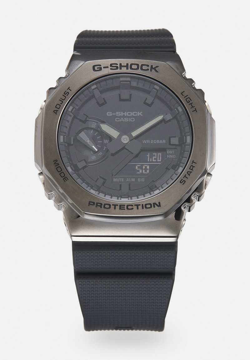 Montre G-SHOCK avec un bracelet en caoutchouc noir et un cadran foncé, dotée d'accents en argent, d'un affichage numérique et d'une lunette en métal protectrice.