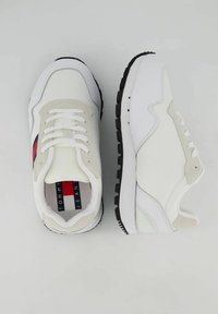 Sneaker bianchi con accenti beige, parte superiore in tessuto liscio, chiusura con lacci, suola in gomma nera e strisce rosse e blu sui lati.