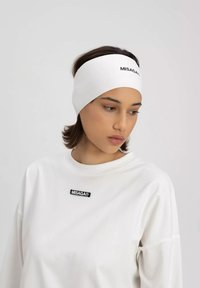 Biała opaska na głowę o gładkiej fakturze z czarnym logo "MISAGA". Noszona z dopasowaną, białą koszulą o luźnym kroju z naszywką logo.