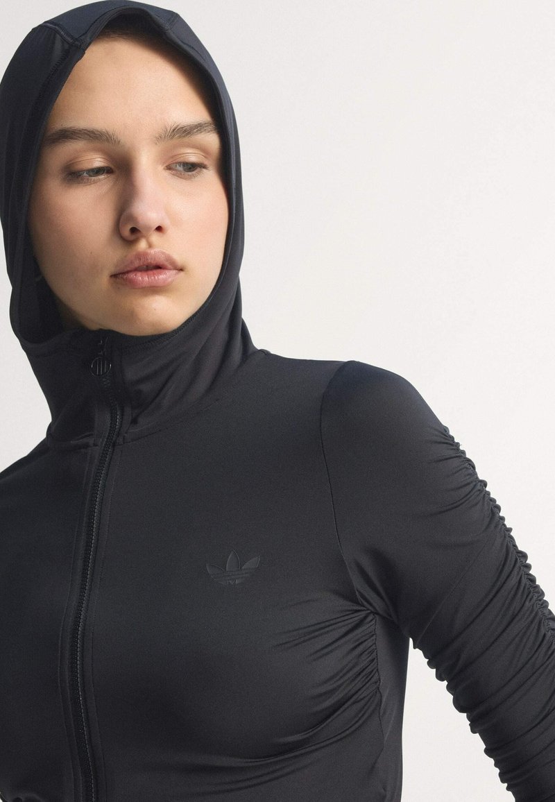 Giacca nera con zip dal design aderente, cappuccio e dettagli arricciati sulle maniche. Presenta un logo discreto sul petto. Realizzata in materiale liscio.